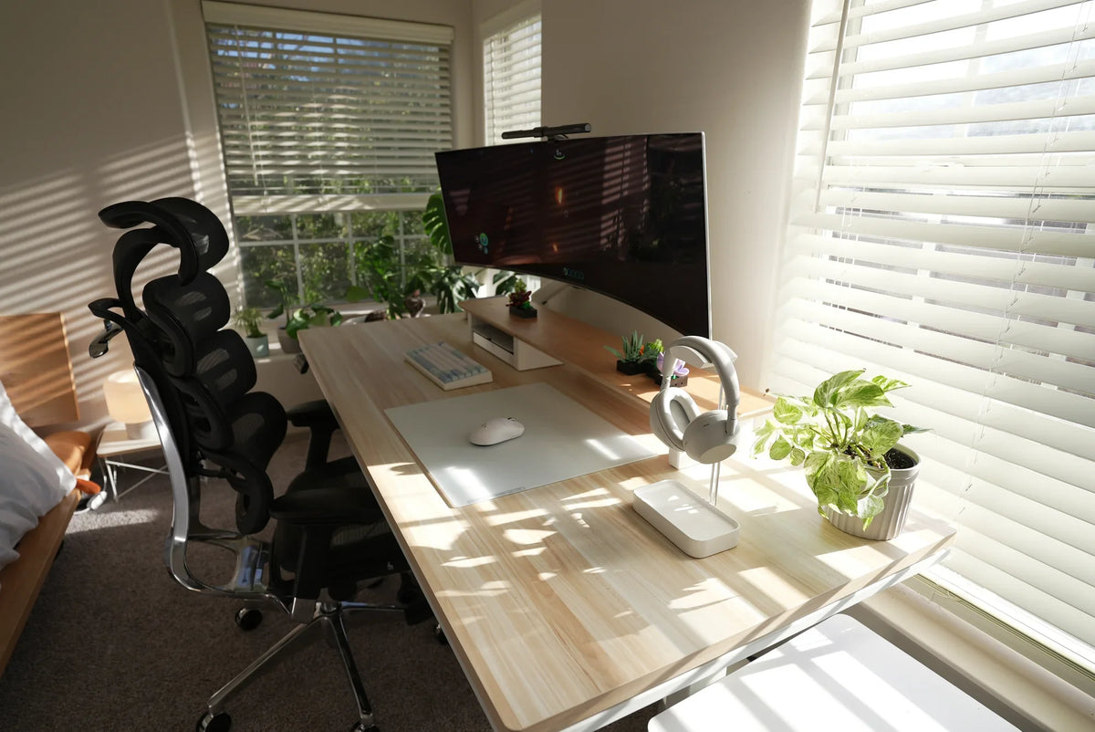 Sunlit bedroom workspace with computer desk beside windows, OdinLake chair, and the edge of a bed