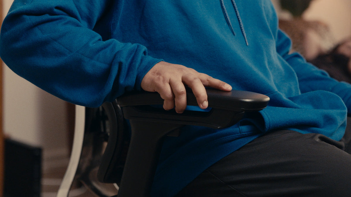 Person resting a hand and forearm lightly on an adjustable office chair armrest