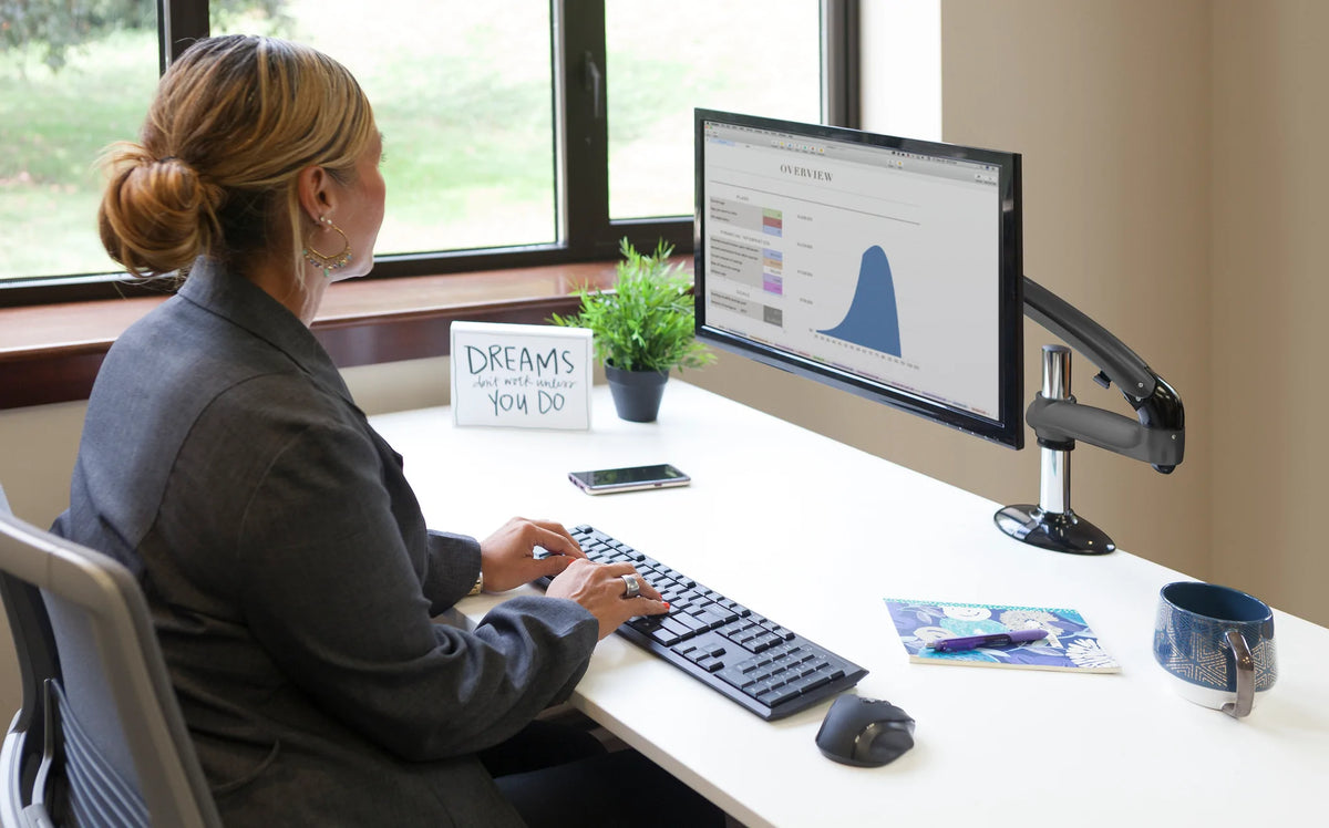 Desktop monitor supported by an adjustable arm in a bright office workspace
