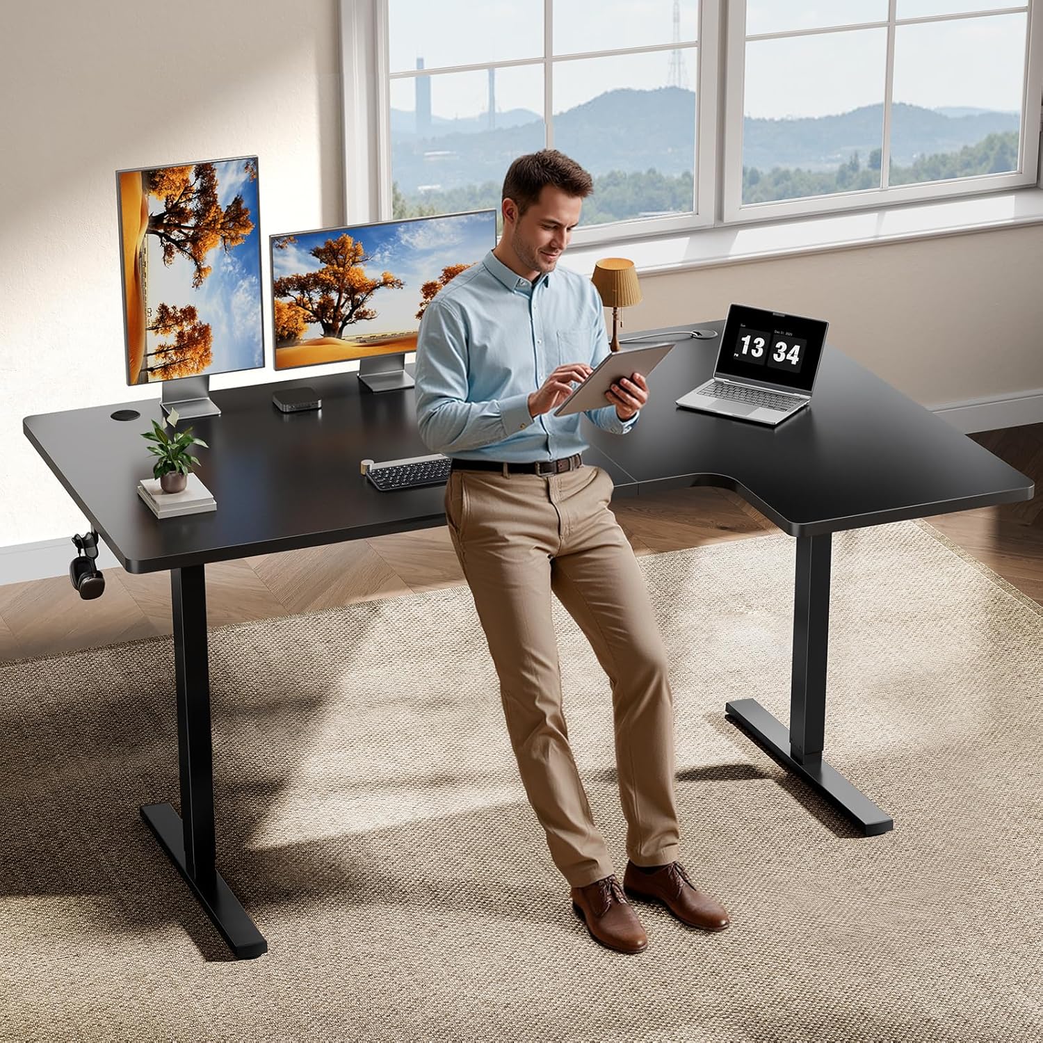 User standing at a black OdinLake L-shaped desk with monitors centered on one wing and a laptop on the return